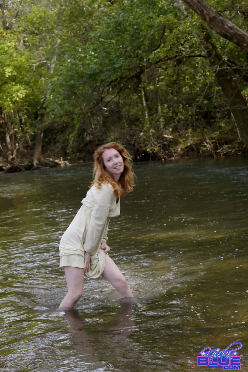 Natural redhead Nicki Blue shows some leg while wading into a shallow stream